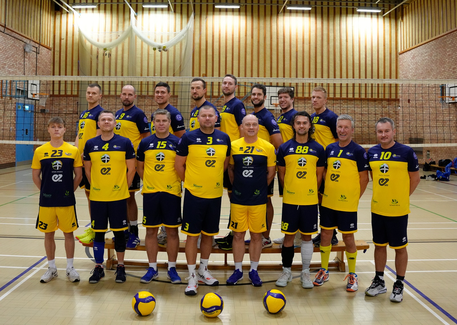 Newmarket Volleyball Club players lined up in yellow and navy kit with three volleyballs